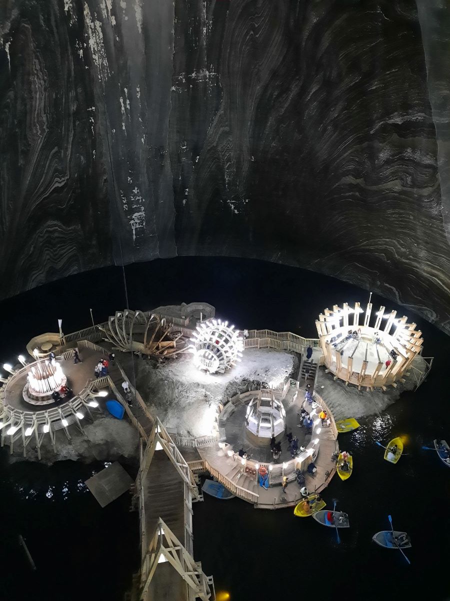 Blick auf den Tereza-Stollen der Salzmine Turda in Rumaenien. Der Stollen ist mit Wasser gefuellt, auf dem gelbe und blaue Ruderboote sind. Beleuchtete Konstruktionen leuchten hell in die Dunkelheit.