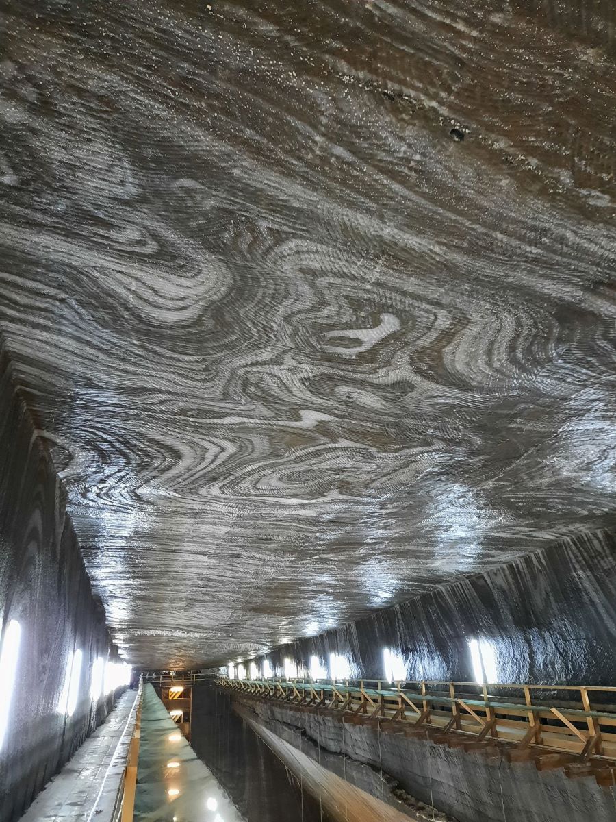 das Bild ist auf der Empore der Salzmine Turda in Rumaenien entstanden. Die Decke des Raumes ist dunkelgrau, von hellgrauen und weißen sich windenden Linien durchzogen. Die Empore ist aus hellem Holz.