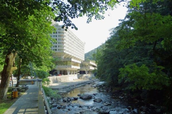 Modernes Hotelgebäude in Băile Herculane, Rumänien – Kontrast zwischen Kurarchitektur, Fluss und bewaldeten Hügeln