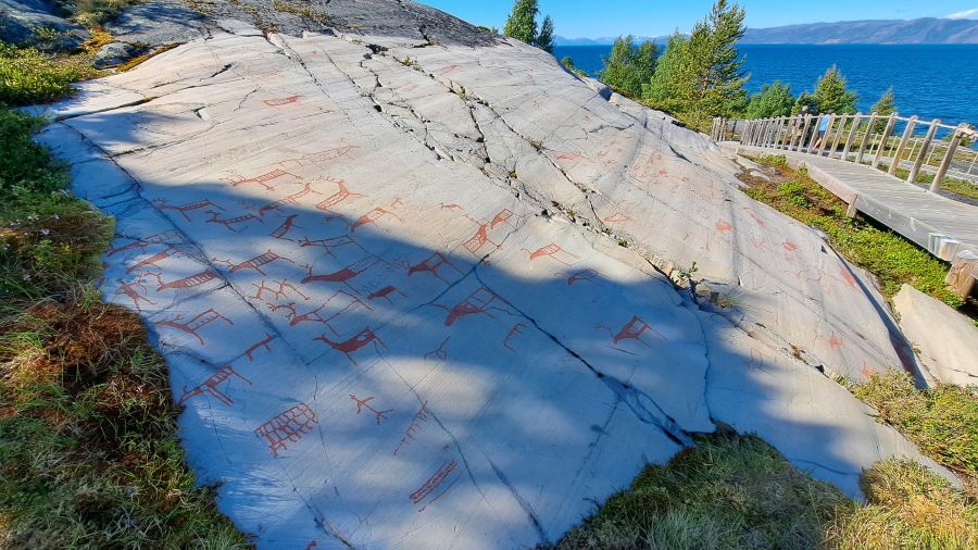 Rot bemalte Felsritzungen auf einer großen Felsplatte am Alta-Museum mit Blick auf den Fjord