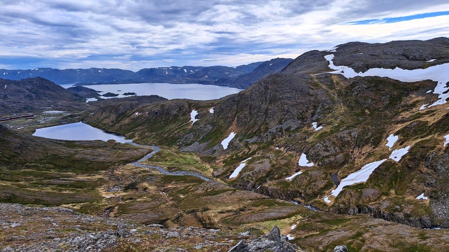 Blick von oben auf ein Tal mit Bergseen und Schneefeldern in der Finnmark, Norwegen