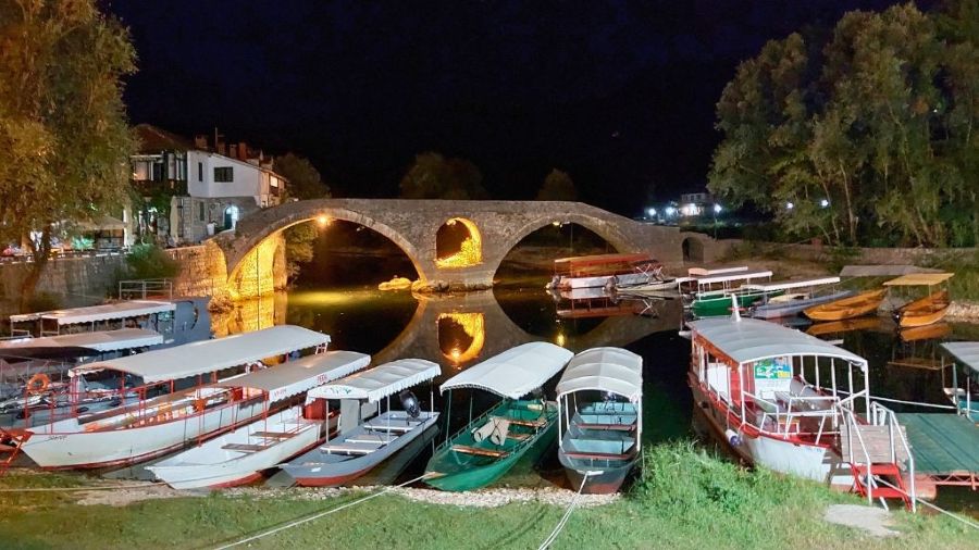 Beleuchtete Steinbrücke von Rijeka Crnojevića bei Nacht mit Ausflugsbooten