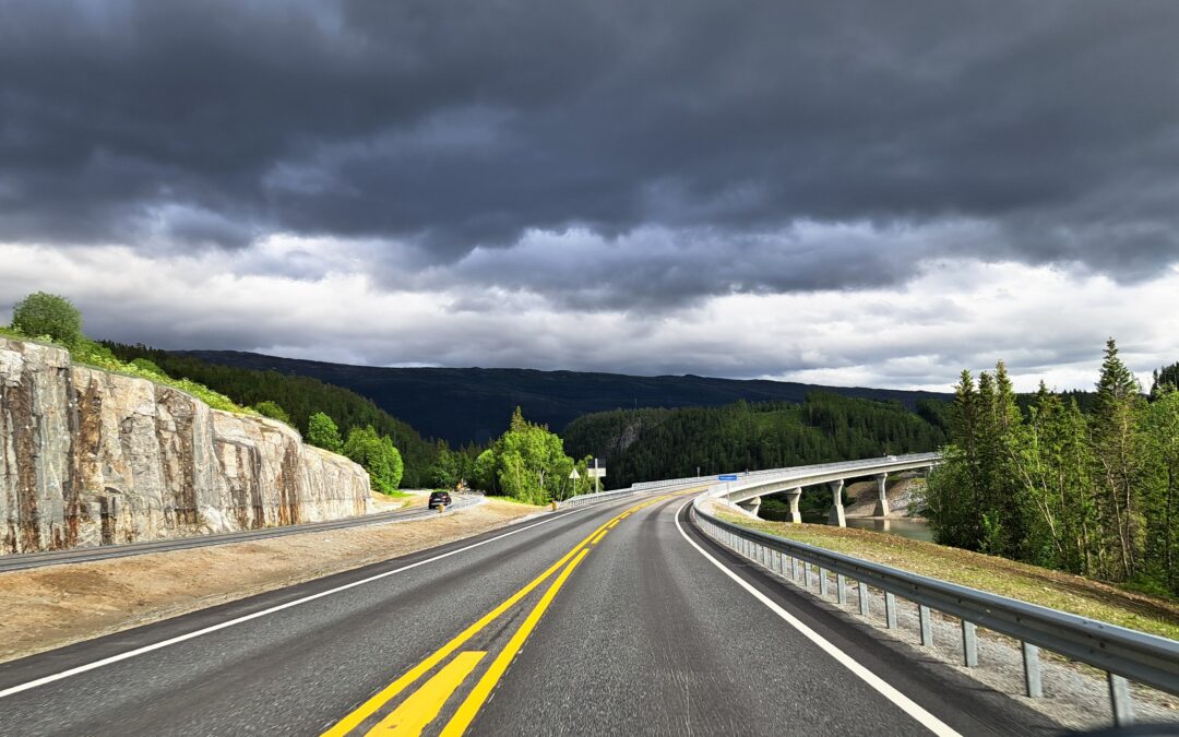 E6 in Norwegen durch bewaldete Berglandschaft unter dunklen Regenwolken