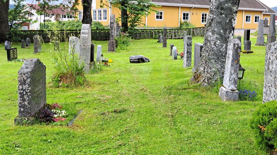 Rasenmähroboter zwischen den Grabsteinen auf dem Friedhof der Ranem Kirche