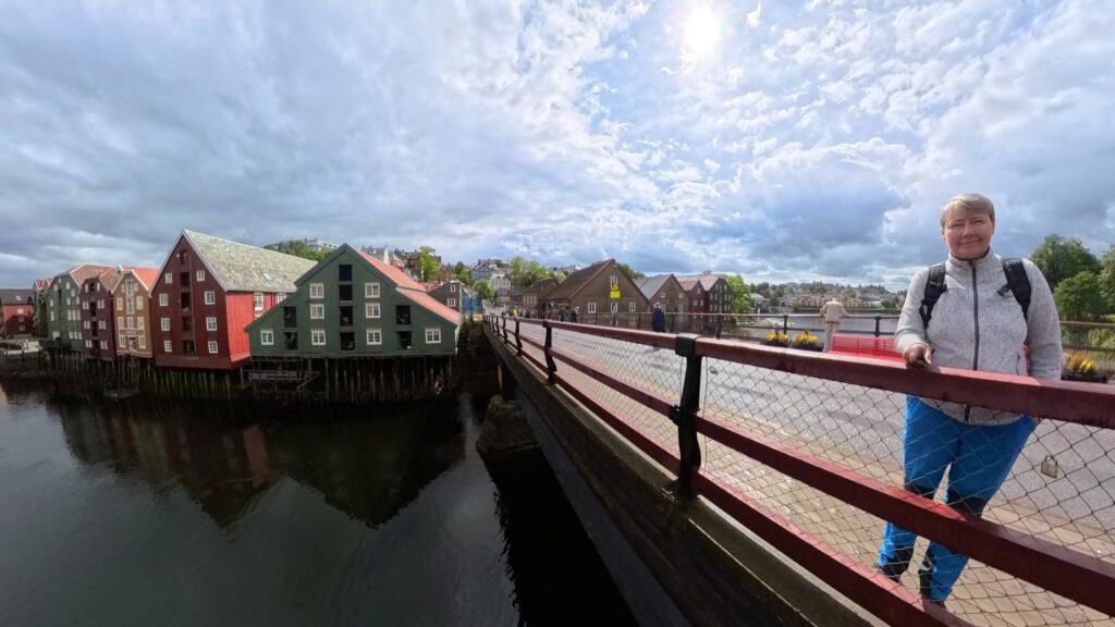 Frau auf der roten Brücke. Im Hintergrund bunte historische Speicherhäuser an der Nidelva in Trondheim